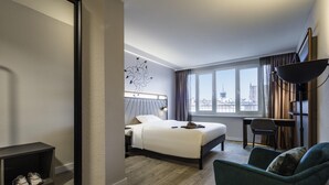 A hotel room with a bed, a desk, a chair, a large window, and a city view. - ibis Styles Bielefeld (Bielefeld)