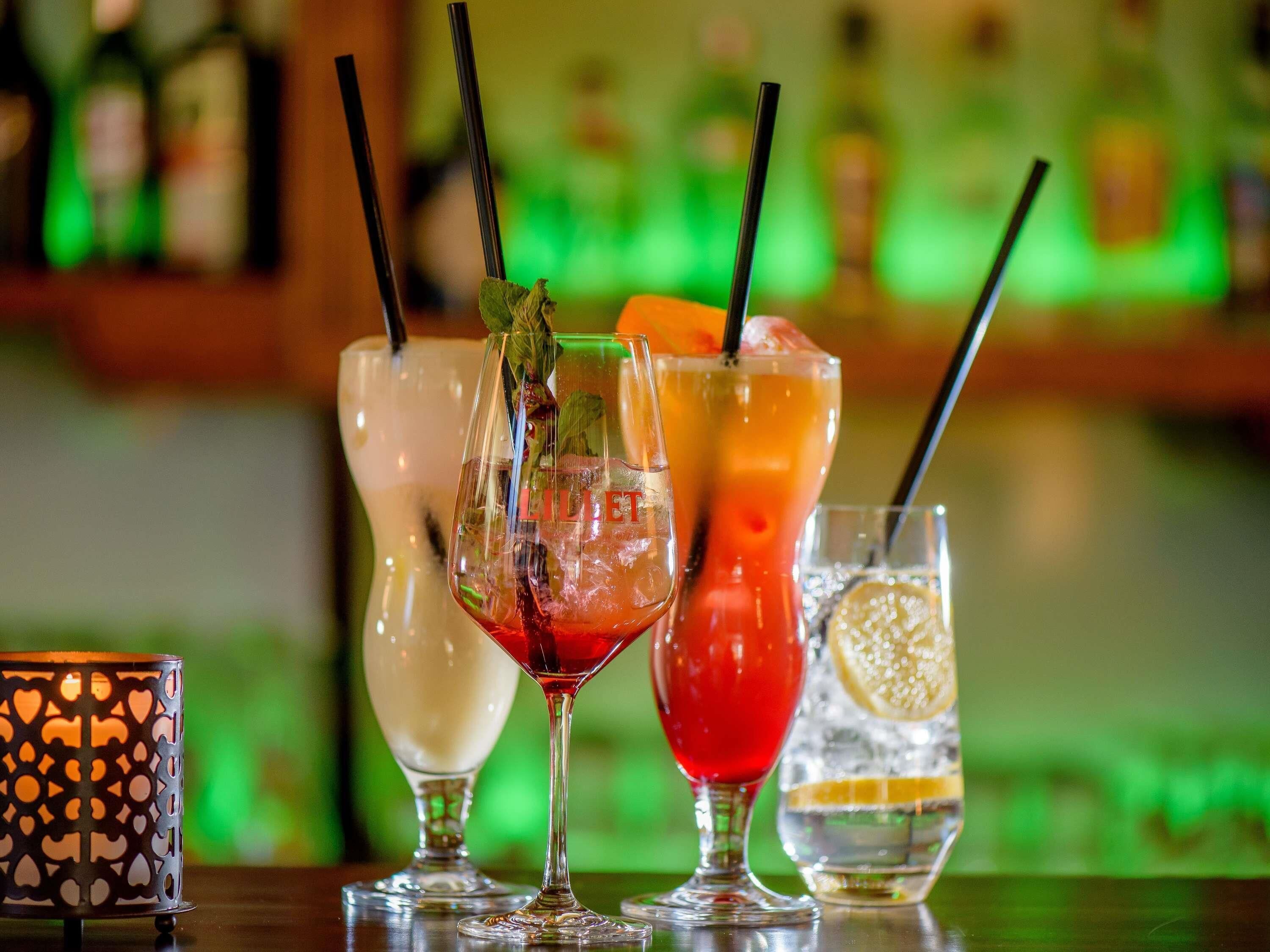 Eine Bar mit verschiedenen Getränken, darunter ein roter Cocktail, ein weißes Getränk und ein klares Getränk mit einer Zitronenscheibe.