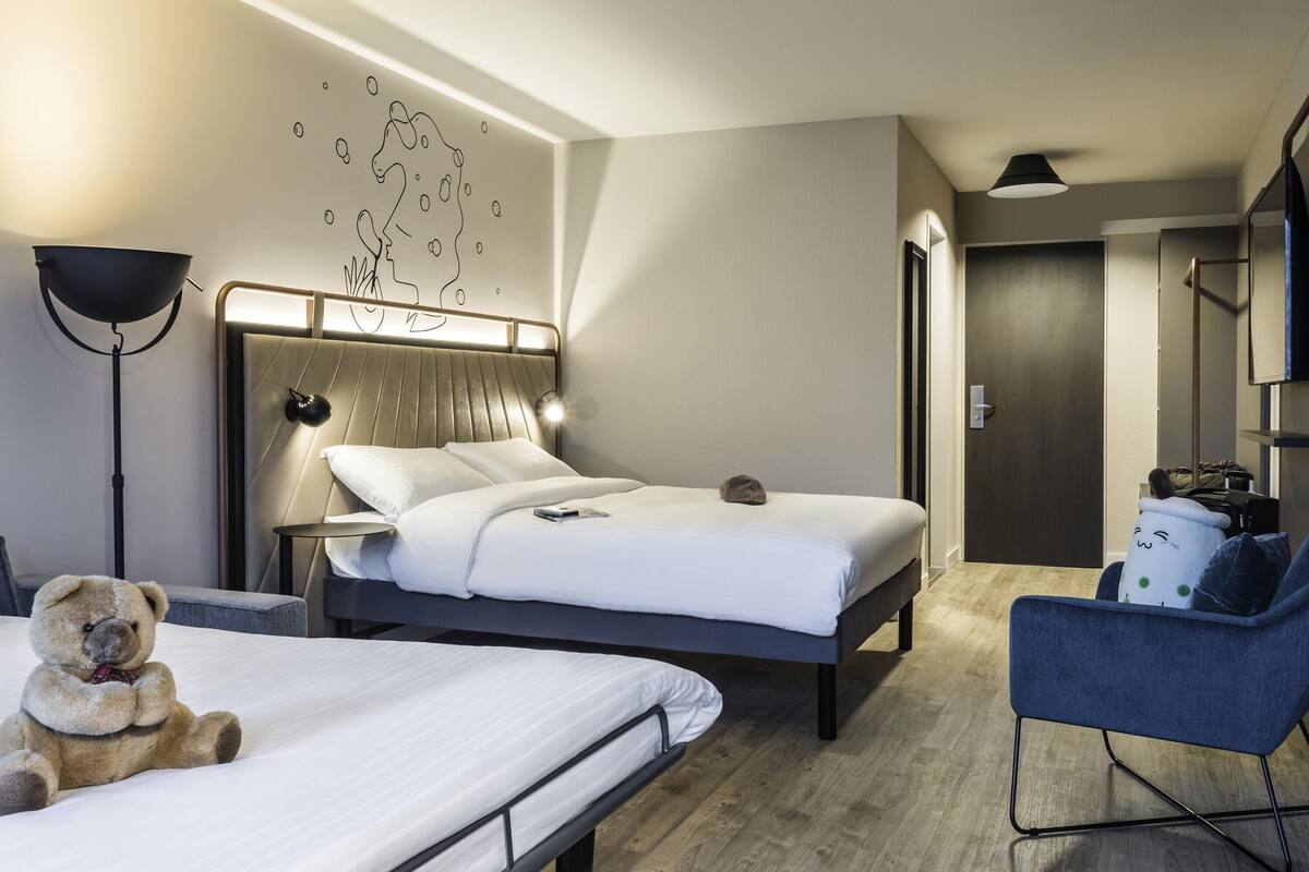 A modern hotel room with a bed, bedside table, lamp, and a chair.