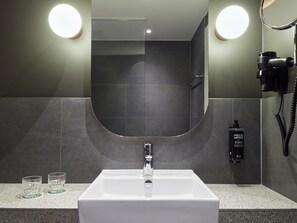 Un baño con un lavamanos blanco, dos luces redondas, un secador de pelo y una botella de champú.