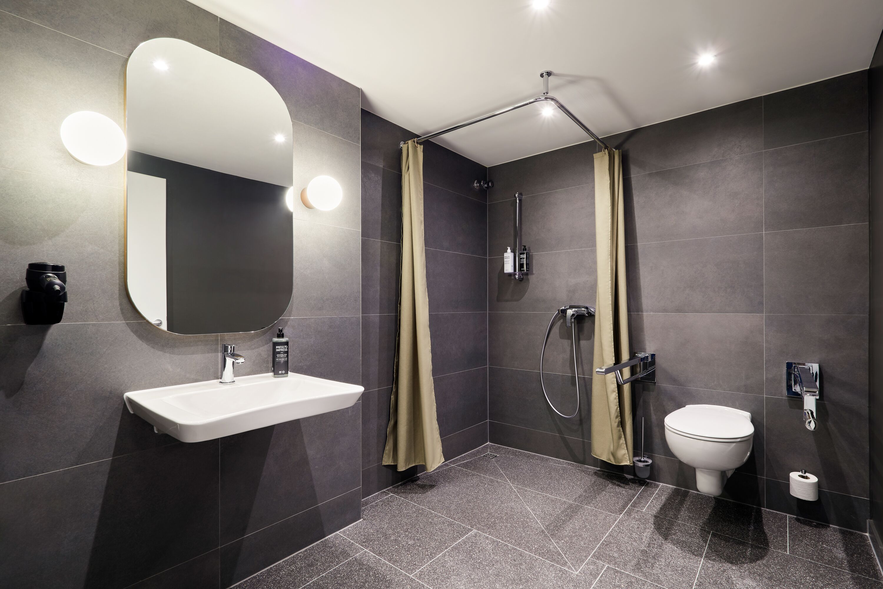 Un baño moderno con un lavamanos blanco, un espejo grande, un inodoro y una zona de ducha.