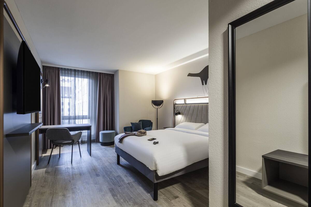 A hotel room with a bed, desk, chair, and a TV.