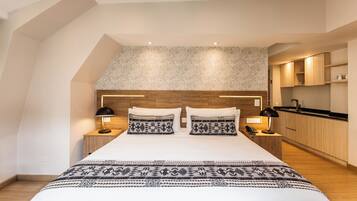 Une chambre moderne avec un grand lit, deux tables de chevet avec des lampes, une tête de lit en bois et un coin cuisine intégré.