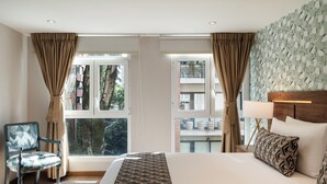 Una habitación de hotel con una cama grande, una silla, un ventanal con cortinas, un cabecero con lámpara y una pared con diseño.