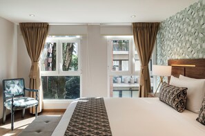 A hotel room with a large bed, a chair, a window with curtains, a headboard with a lamp, and a patterned wall. - Hotel Portón de la Cabrera (Bogotá)