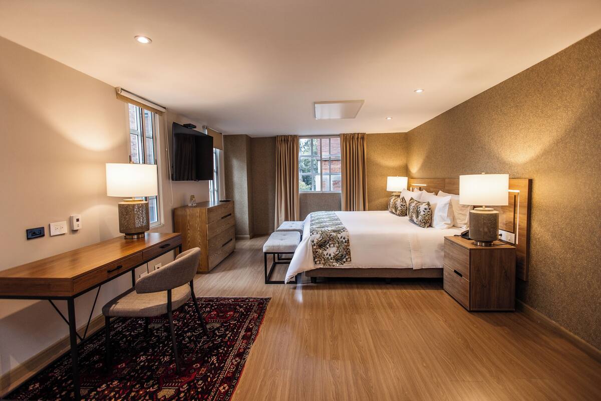 Una habitación de hotel con cama, escritorio, silla y mesitas de noche con lámparas.
