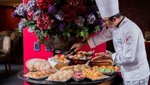 Uno chef serve pasticcini a un buffet, con un'armoniosa composizione floreale sullo sfondo.