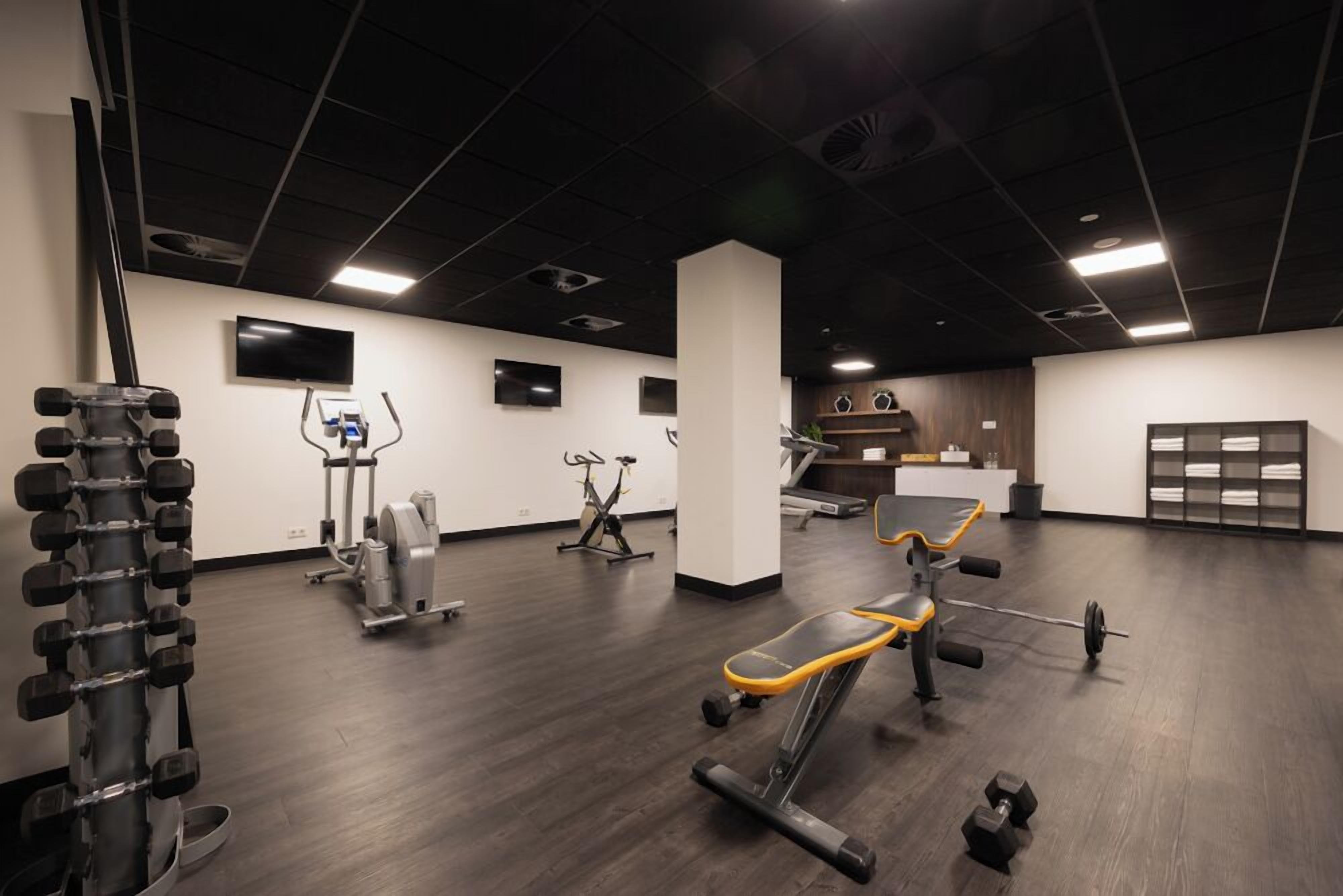 Un gimnasio moderno con diverso equipo de ejercicio, incluyendo mancuernas, una prensa de banca y máquinas de cardio.