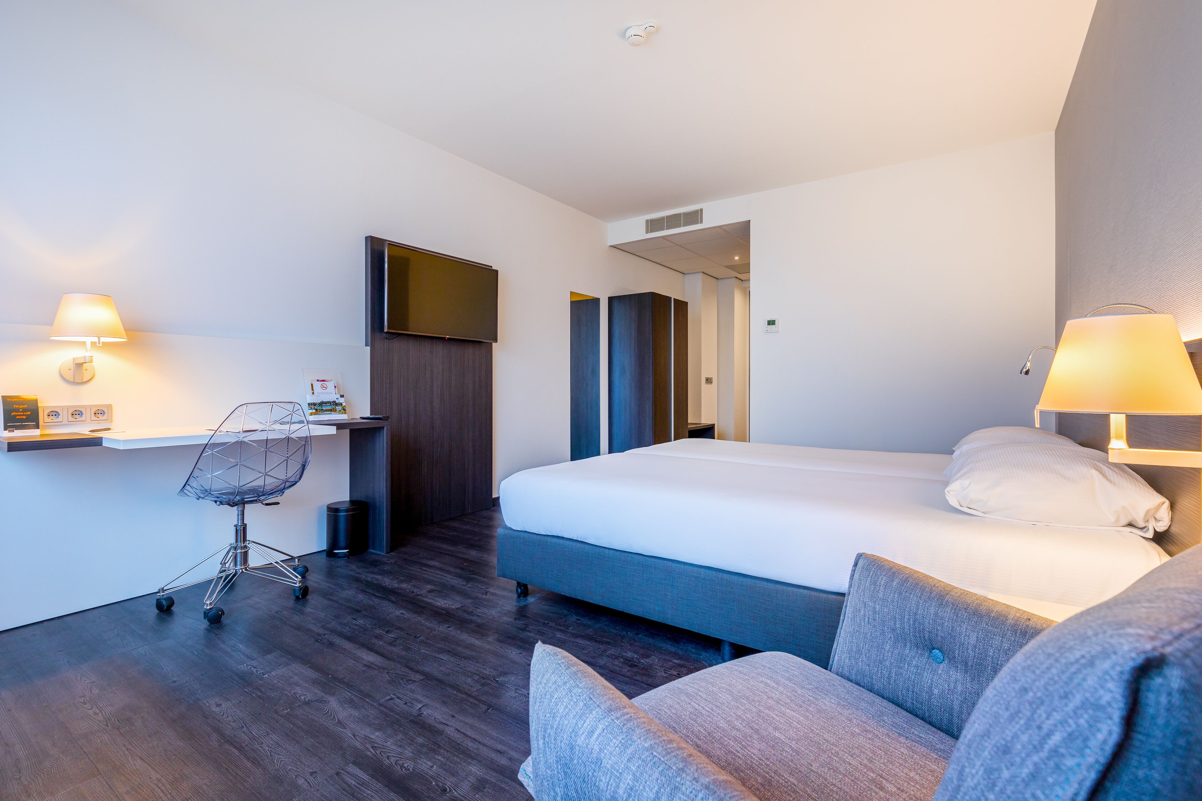 Quarto de hotel moderno com uma cama grande, uma escrivaninha com cadeira e um espaço de estar separado.