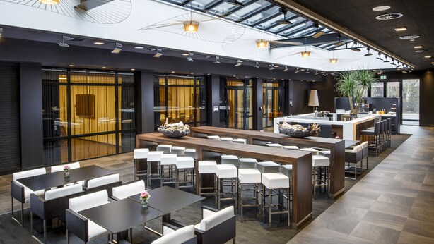 A modern hotel lobby with a long reception desk, multiple seating areas, and a large glass wall providing a view of the outdoors. - Postillion Hotel Dordrecht (Dordrecht)