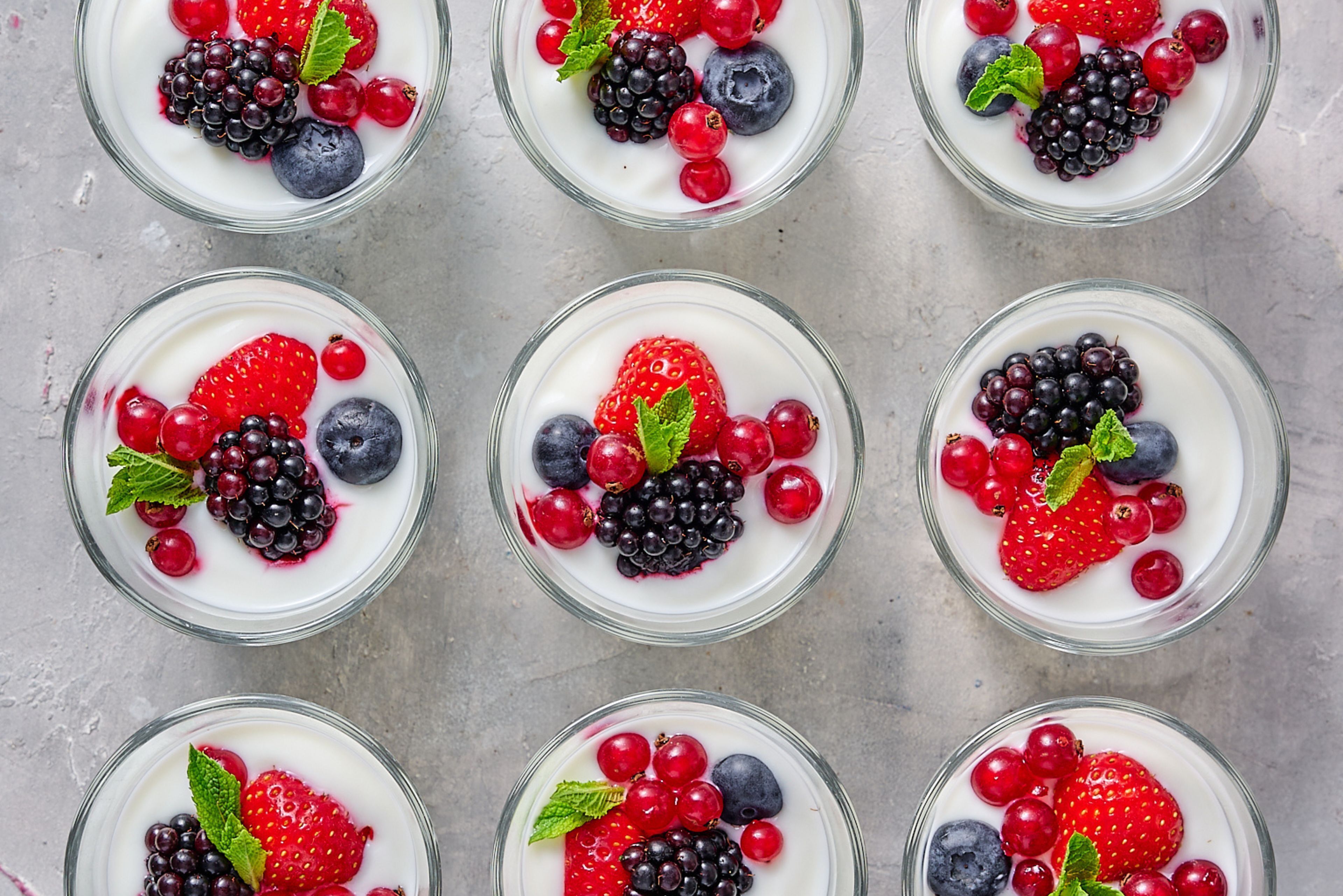 Six bowls of yogurt topped with various berries and mint leaves.