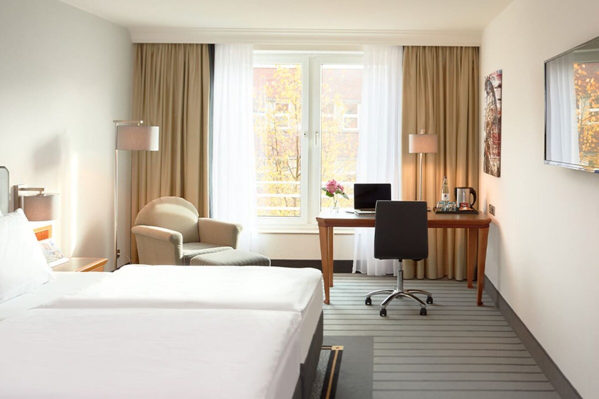 A hotel room with two beds, a desk, a chair, and a window with curtains.