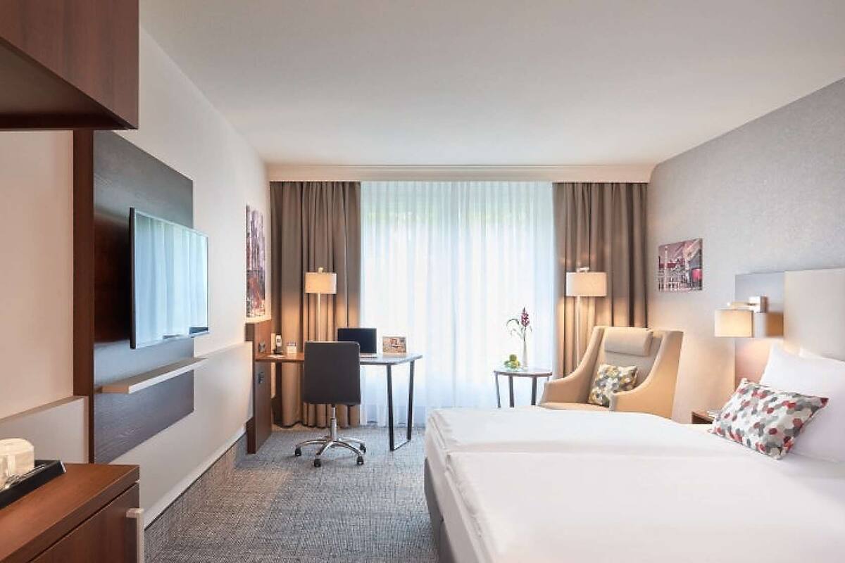 A hotel room with a large bed, a desk, a chair, and a TV.