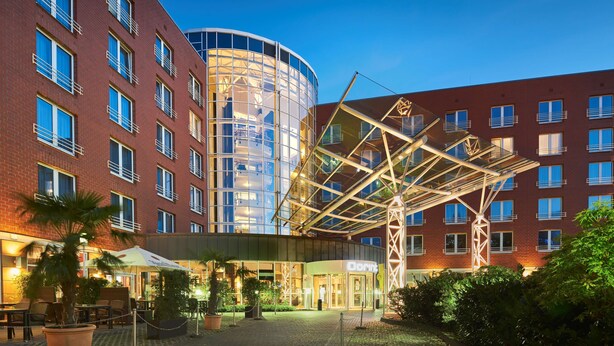 A hotel with a modern glass facade, outdoor seating area, and a covered entrance.