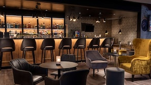A bar area with multiple stools and a bar counter, a seating area with round tables and chairs, and a wall with a television screen.