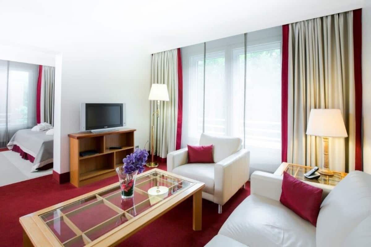 A hotel room with a bed, a TV, a sofa, a coffee table, and a lamp.
