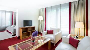 A hotel room with a bed, a TV, a sofa, a coffee table, and a lamp.