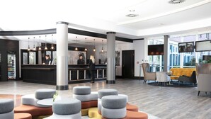 A modern hotel lobby with a reception desk, seating area, and large windows.