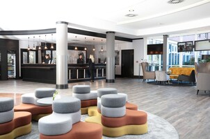 Um saguão moderno de hotel, com balcão de recepção, área de estar e grandes janelas.