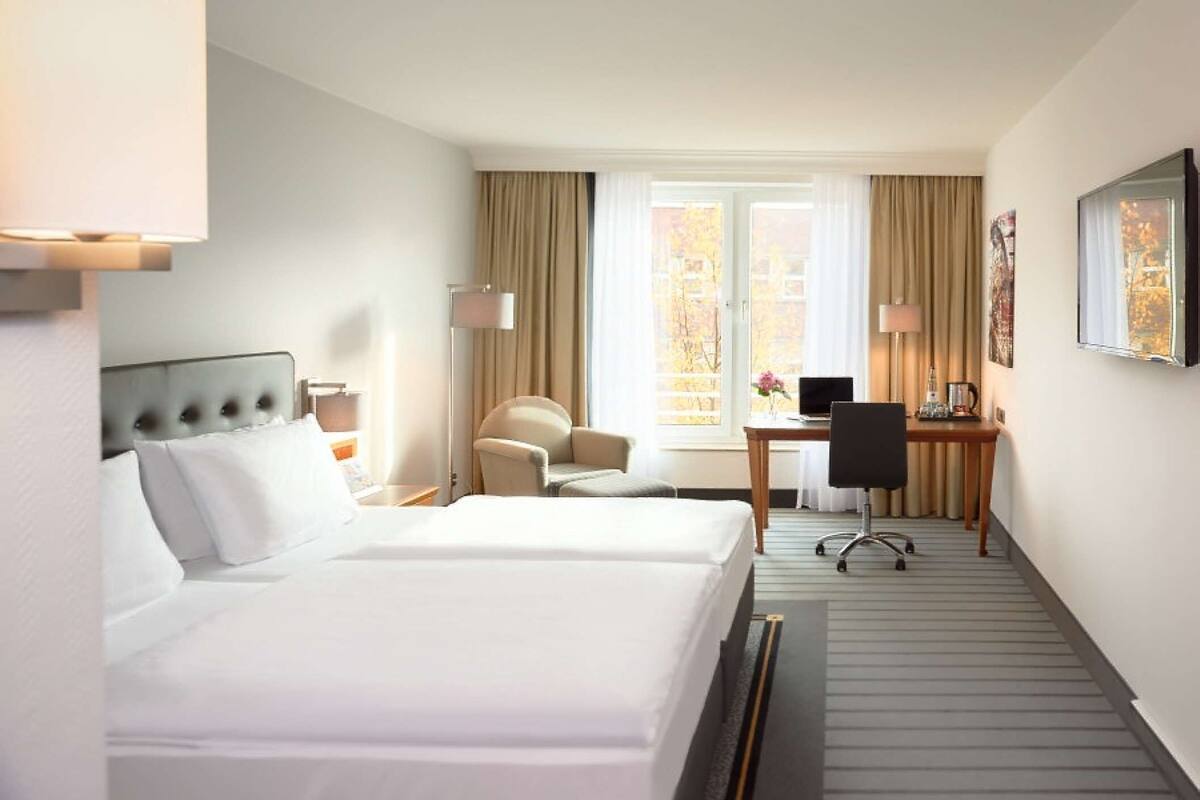 A hotel room with two beds, a desk, a chair, and a window with curtains.