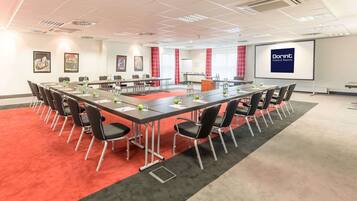 A conference room with a long table, chairs, and a projector screen displaying 'Dornt Hotels & Resorts'.