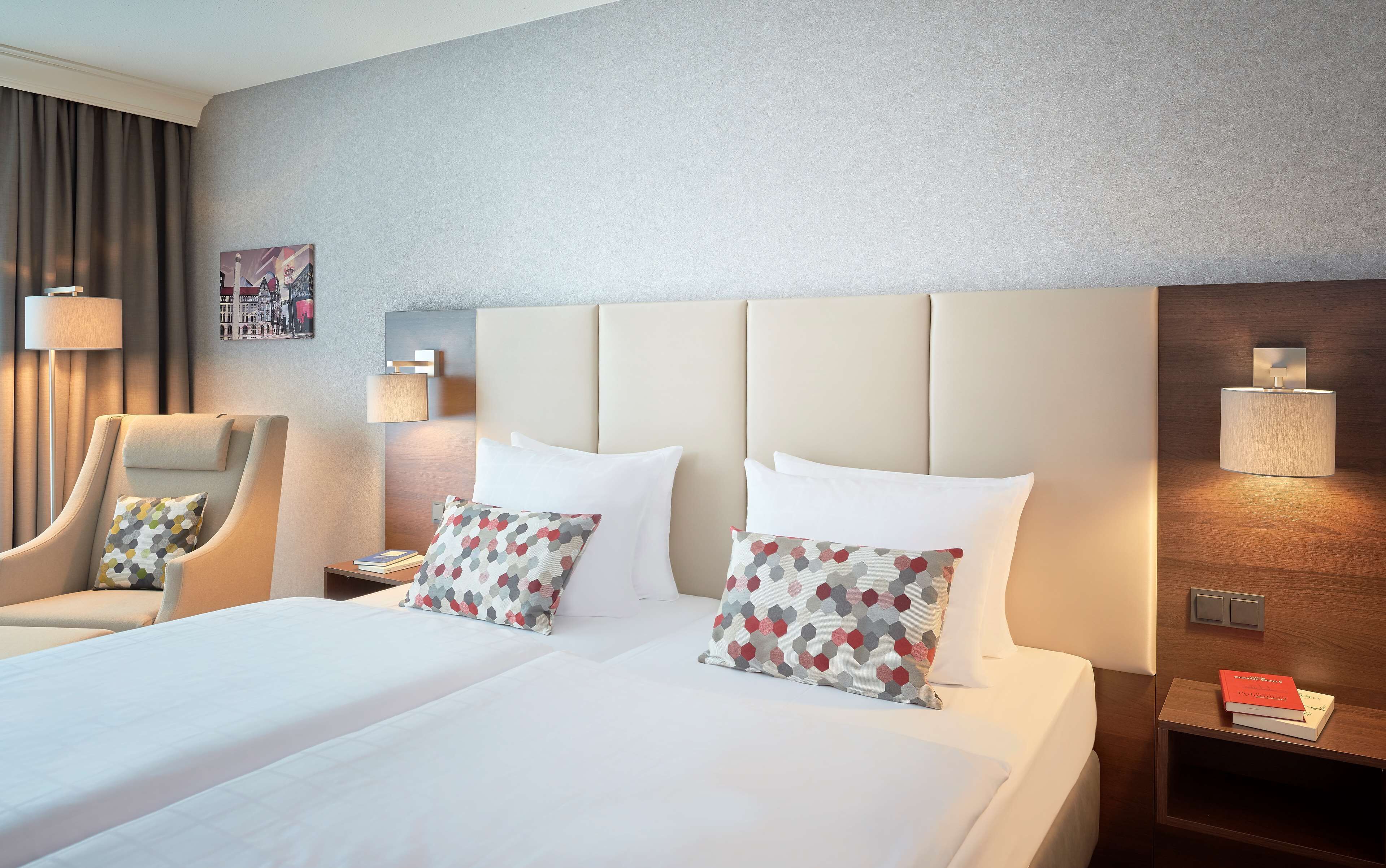 A hotel room with a large bed, two bedside tables, a chair, and a wall-mounted lamp.