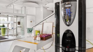 Una cafetera moderna con pantalla digital, puerta de cristal y una mesa con una taza de café y un marco con una fotografía.