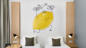Habitación de hotel con dos camas, una obra de arte en la pared de un limón con una bicicleta y lámparas de noche.