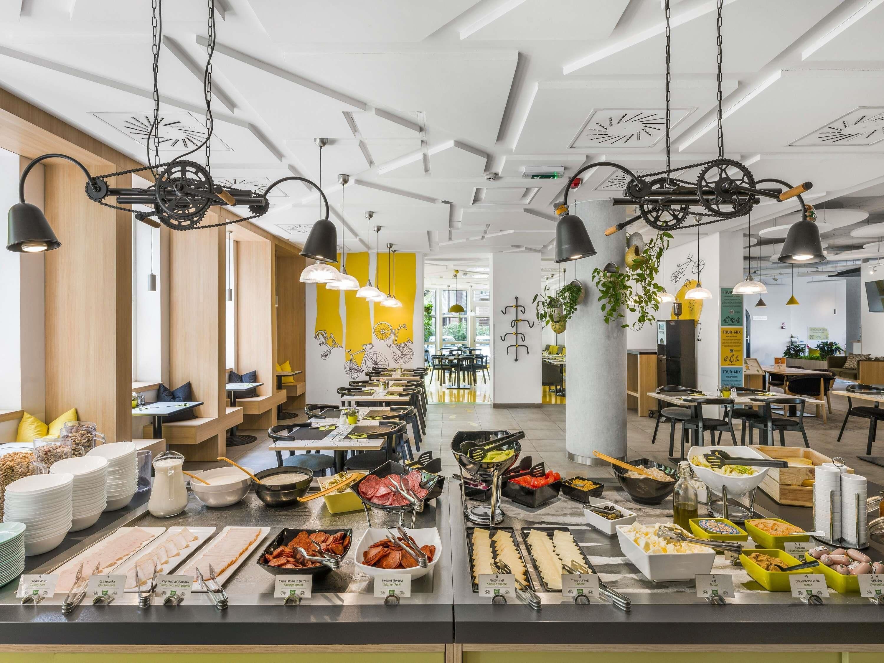 A modern cafeteria with multiple dining areas, a variety of food options, and hanging bicycle-themed decorations.
