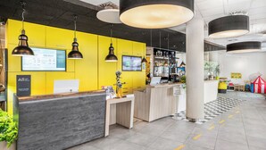 Zona de recepción de hotel con una pared amarillo brillante, un mostrador de recepción y una zona de bar.