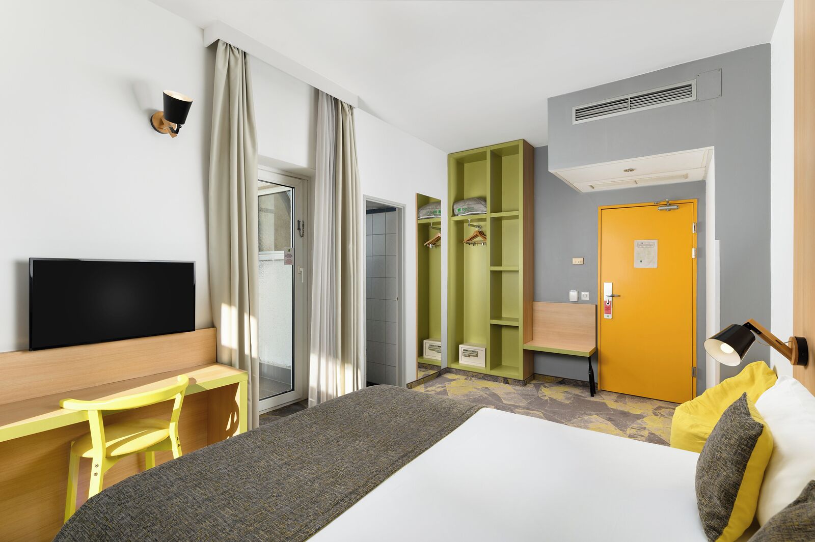 A hotel room with a bed, a desk, a TV, a wardrobe, and a bathroom.