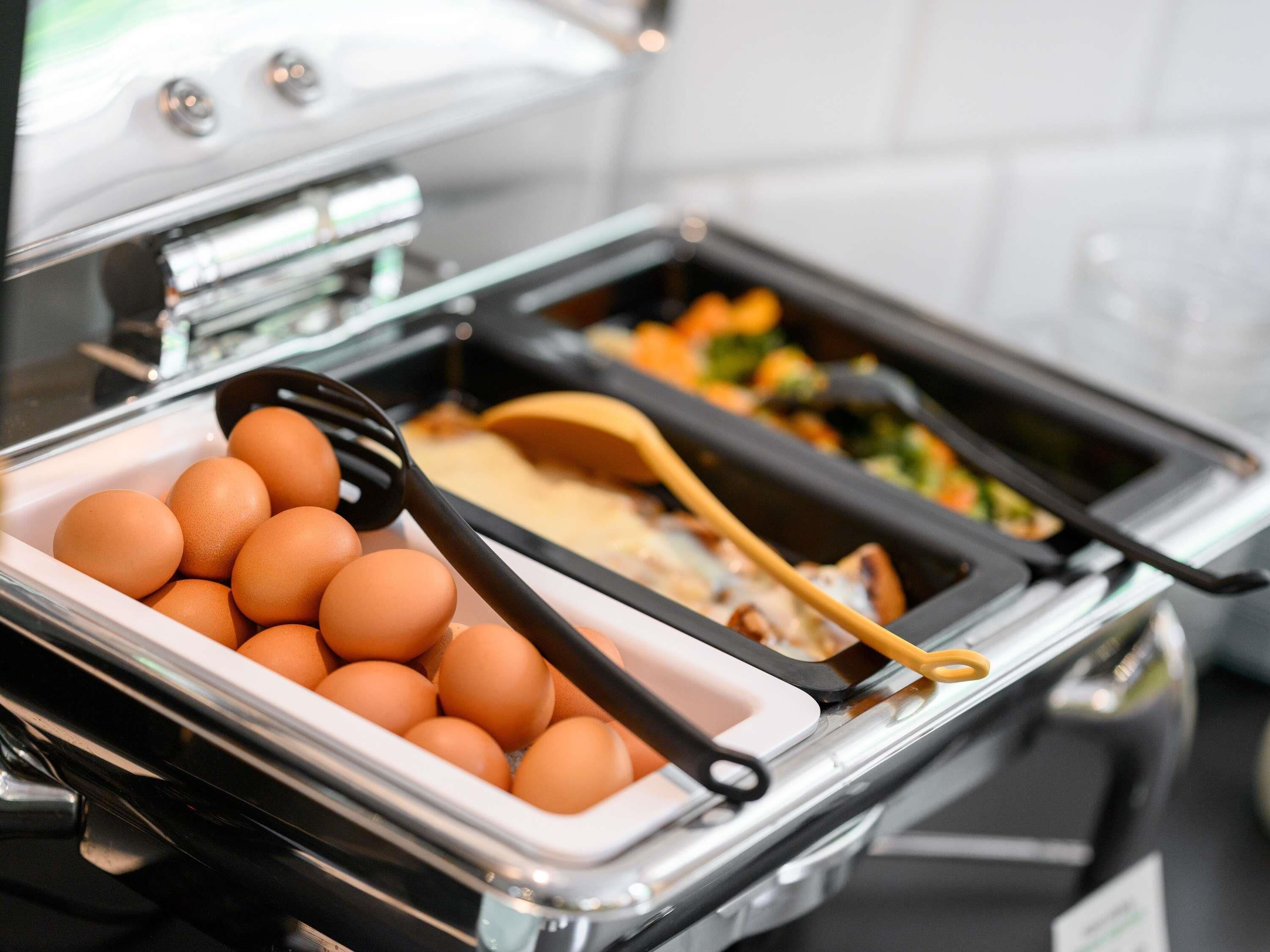 A buffet setup with a container of eggs and a tray of assorted food items.