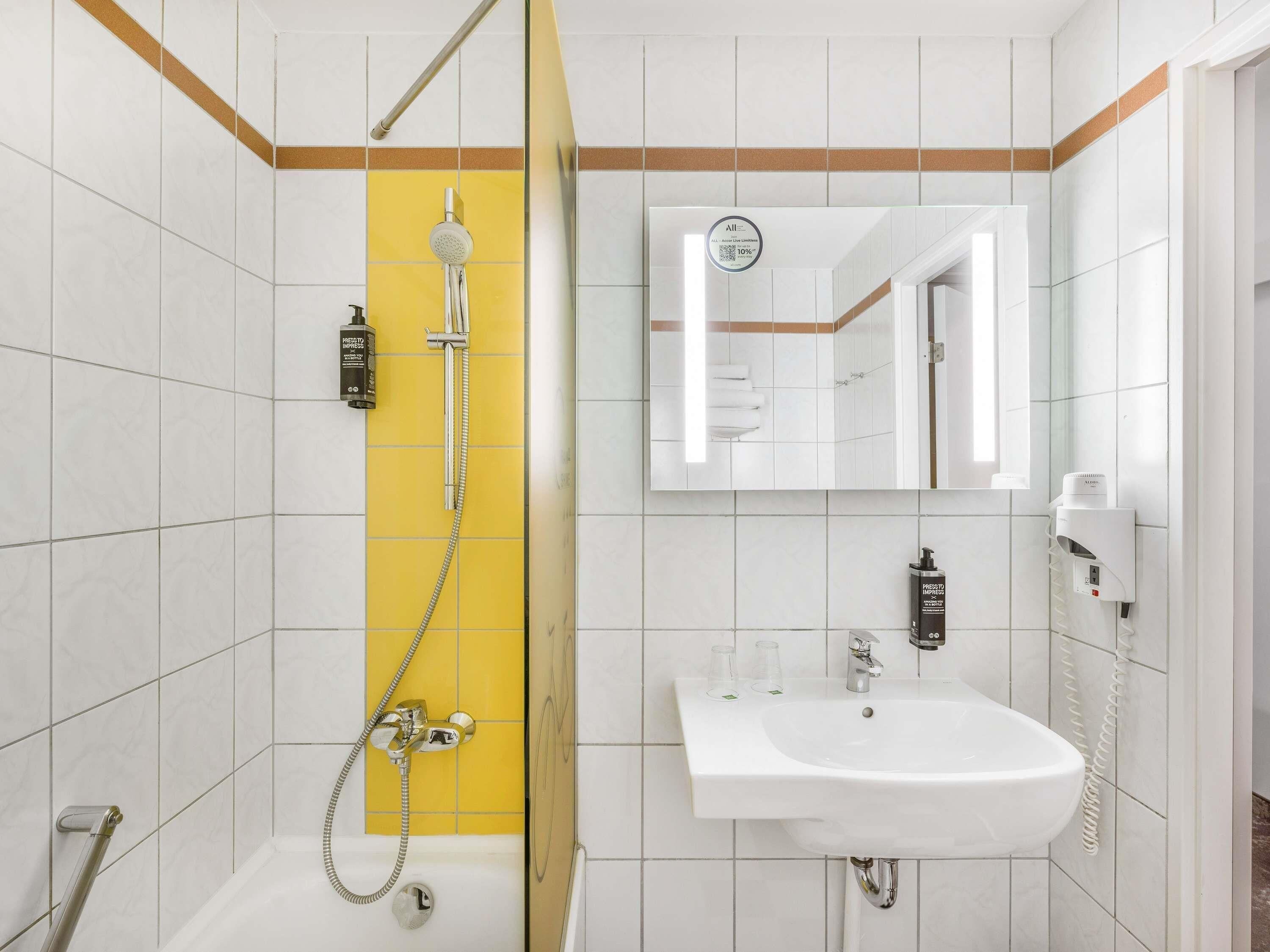 A bathroom with a shower, a sink, a mirror, and a towel rack.