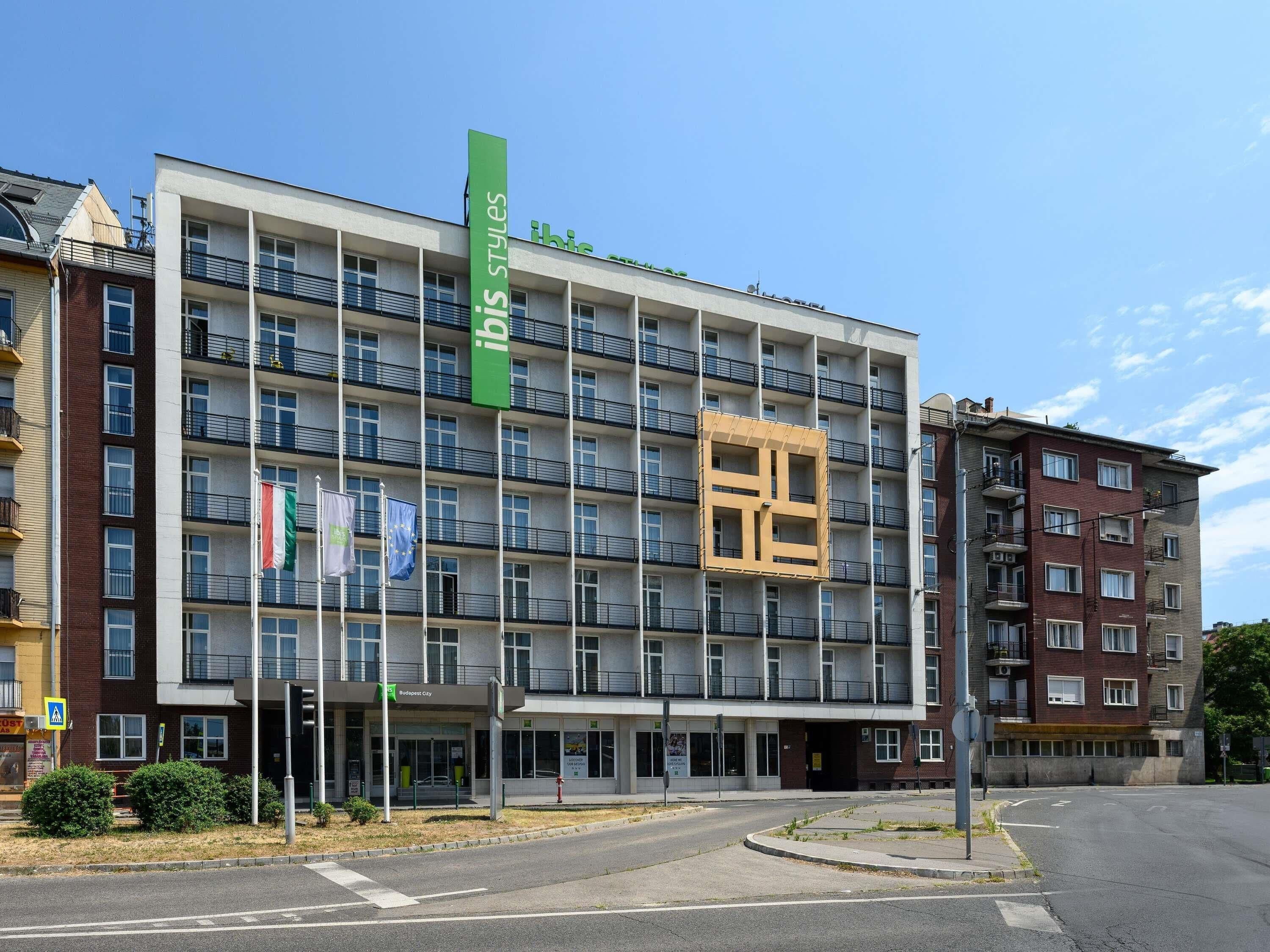 Ett hotell med flera våningar, balkonger, en grön skylt och flaggor.