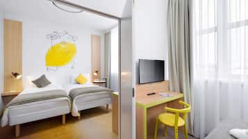 A hotel room with two beds, a desk, a chair, a TV, and a large window with curtains.