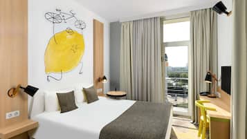 Habitación de hotel con cama, escritorio, silla, ventana con cortinas y un cuadro amarillo en la pared.