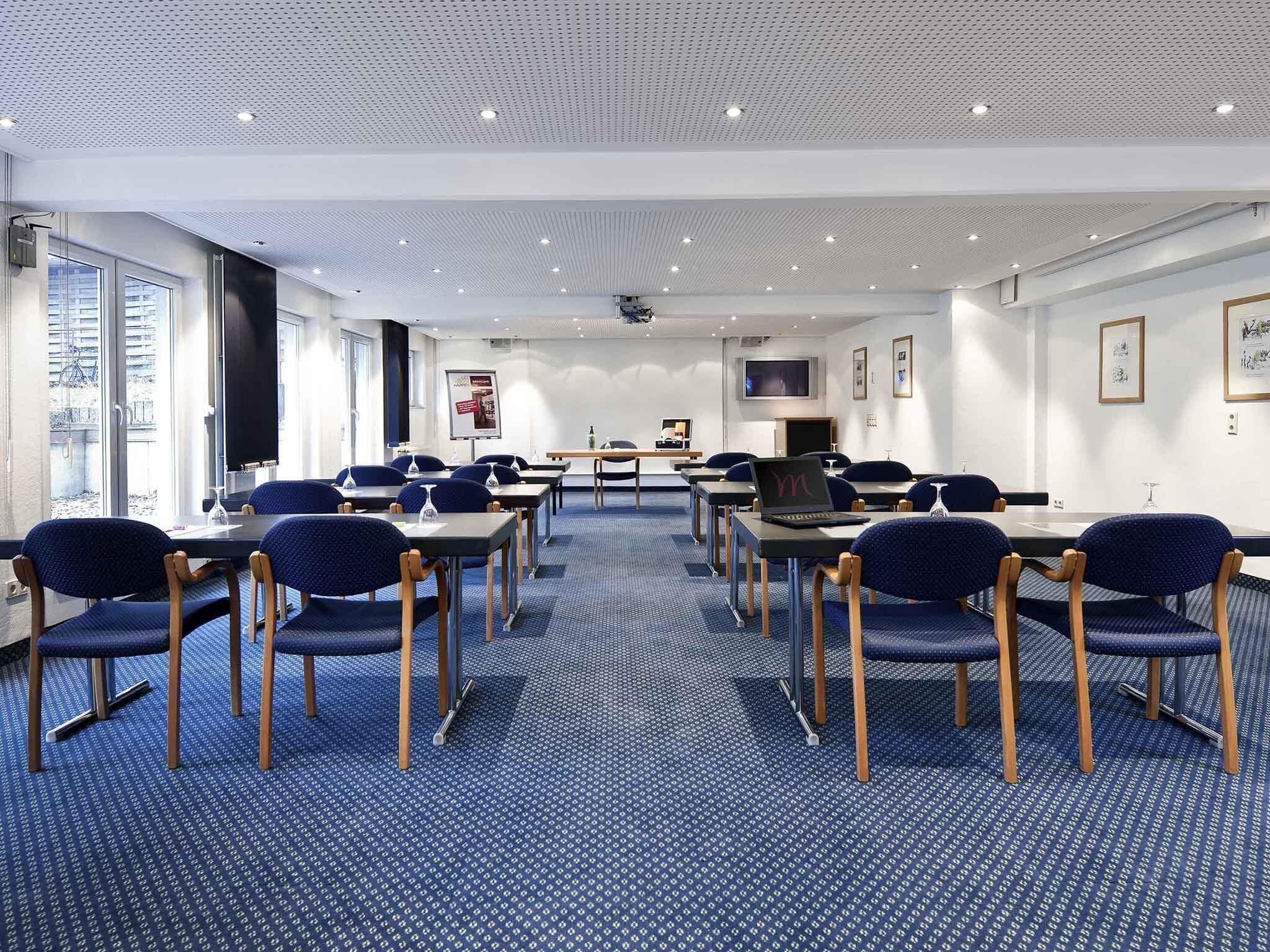 A conference room with tables, chairs, and a projector screen.