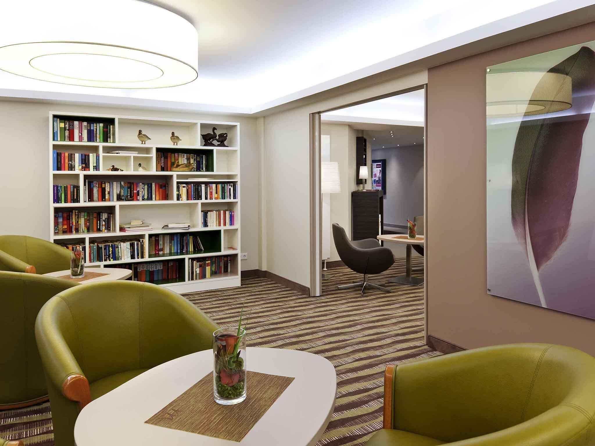A modern hotel room with a large bookshelf, a dining area, and a view into another room.