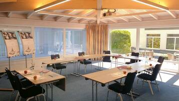 Un salón de conferencias con mesas, sillas, un proyector y ventanas amplias.