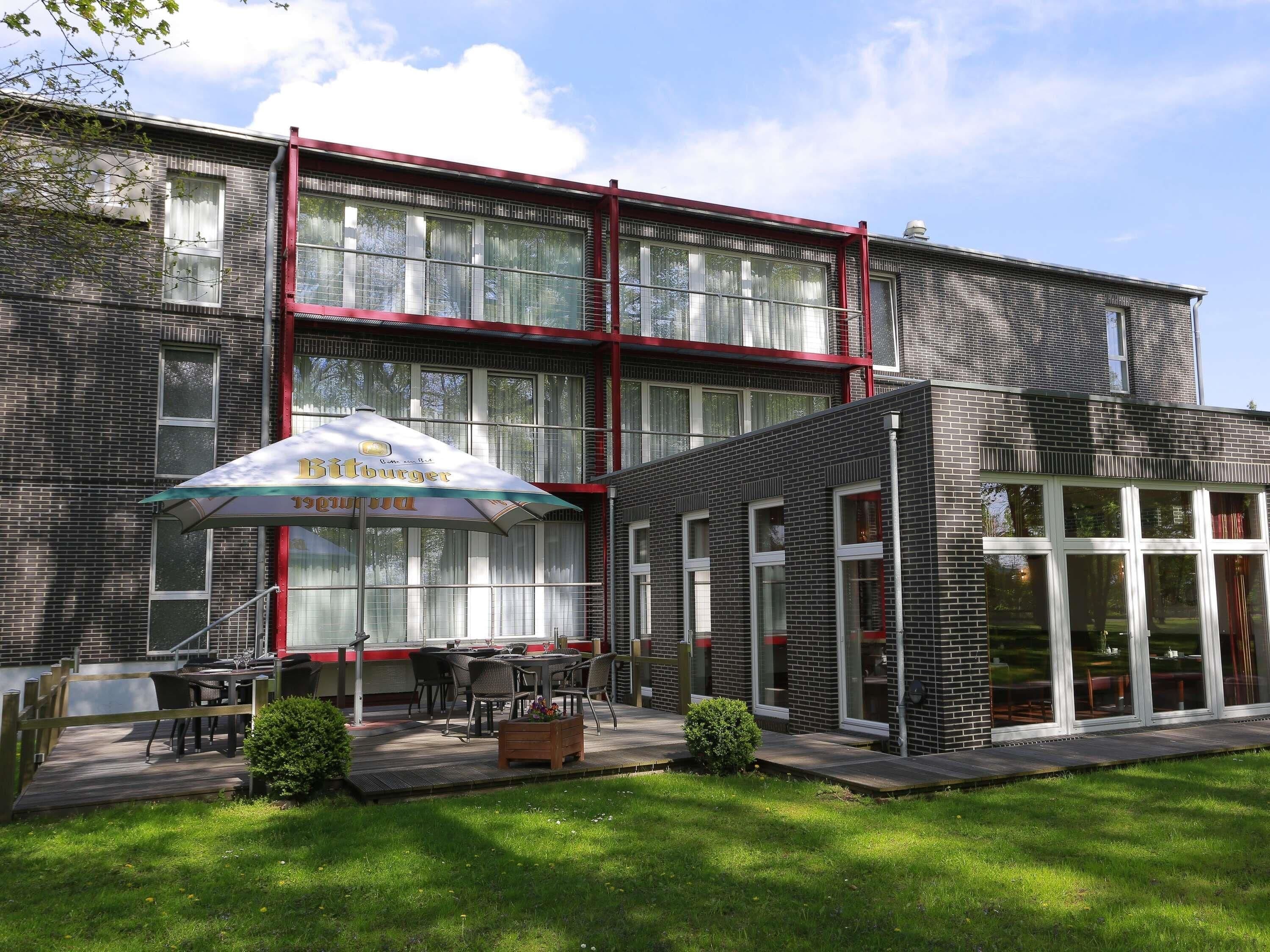 A modern building with a brick facade, large windows, and a covered outdoor seating area with tables and chairs.