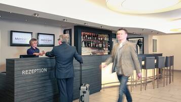 Un espace d’accueil comprenant un comptoir de réception portant l’inscription « RÉCEPTION », un bar avec diverses bouteilles et un coin salon avec des chaises.