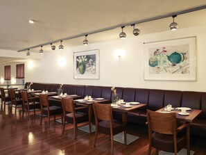 A restaurant with wooden tables and chairs, a long bench, and wall-mounted lighting. - Mercure Hotel Am Entenfang Hannover (Hannover)