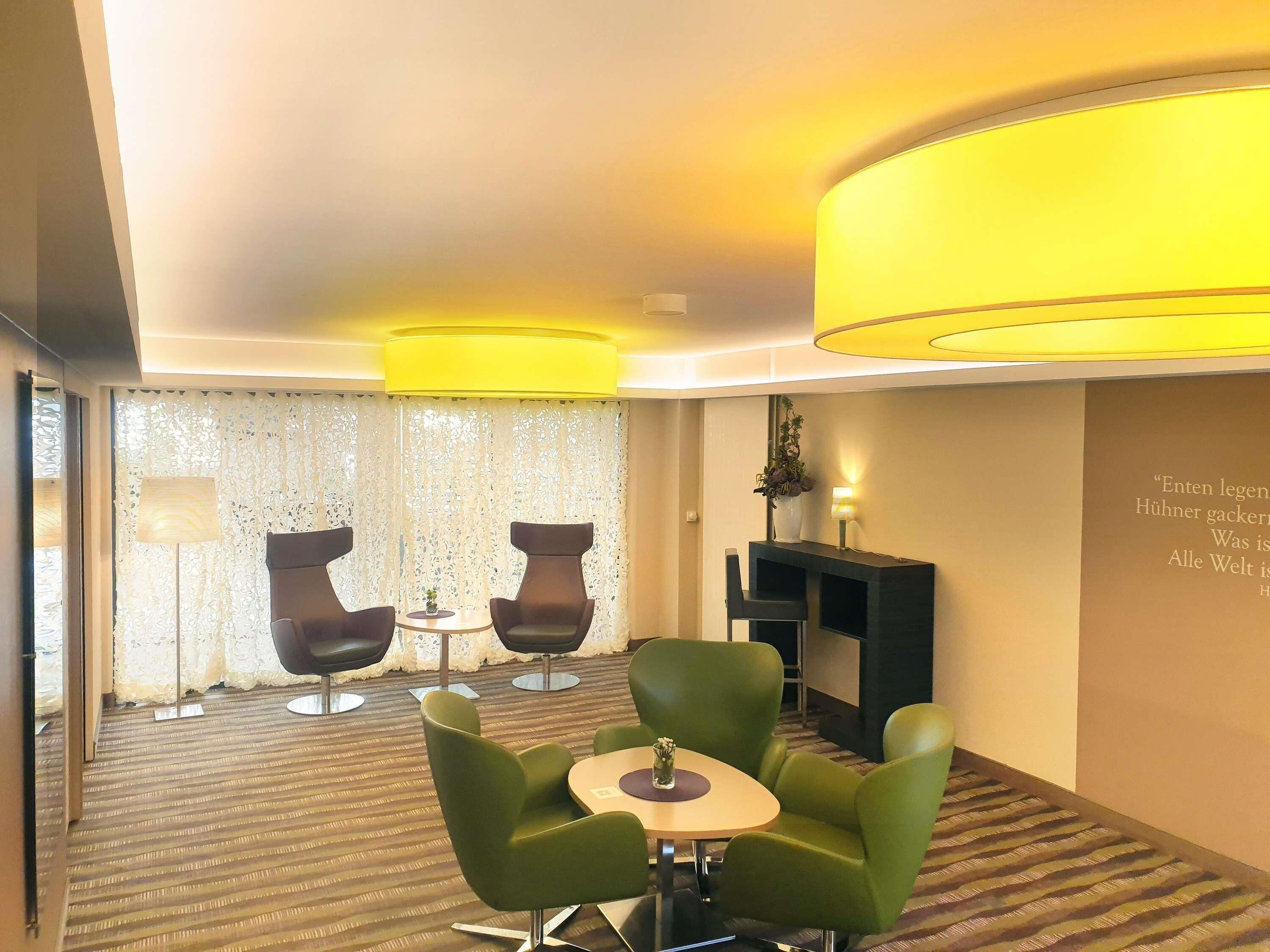 Quarto de hotel com área de estar, cadeiras verdes, uma pequena mesa, lareira e parede decorativa com texto.
