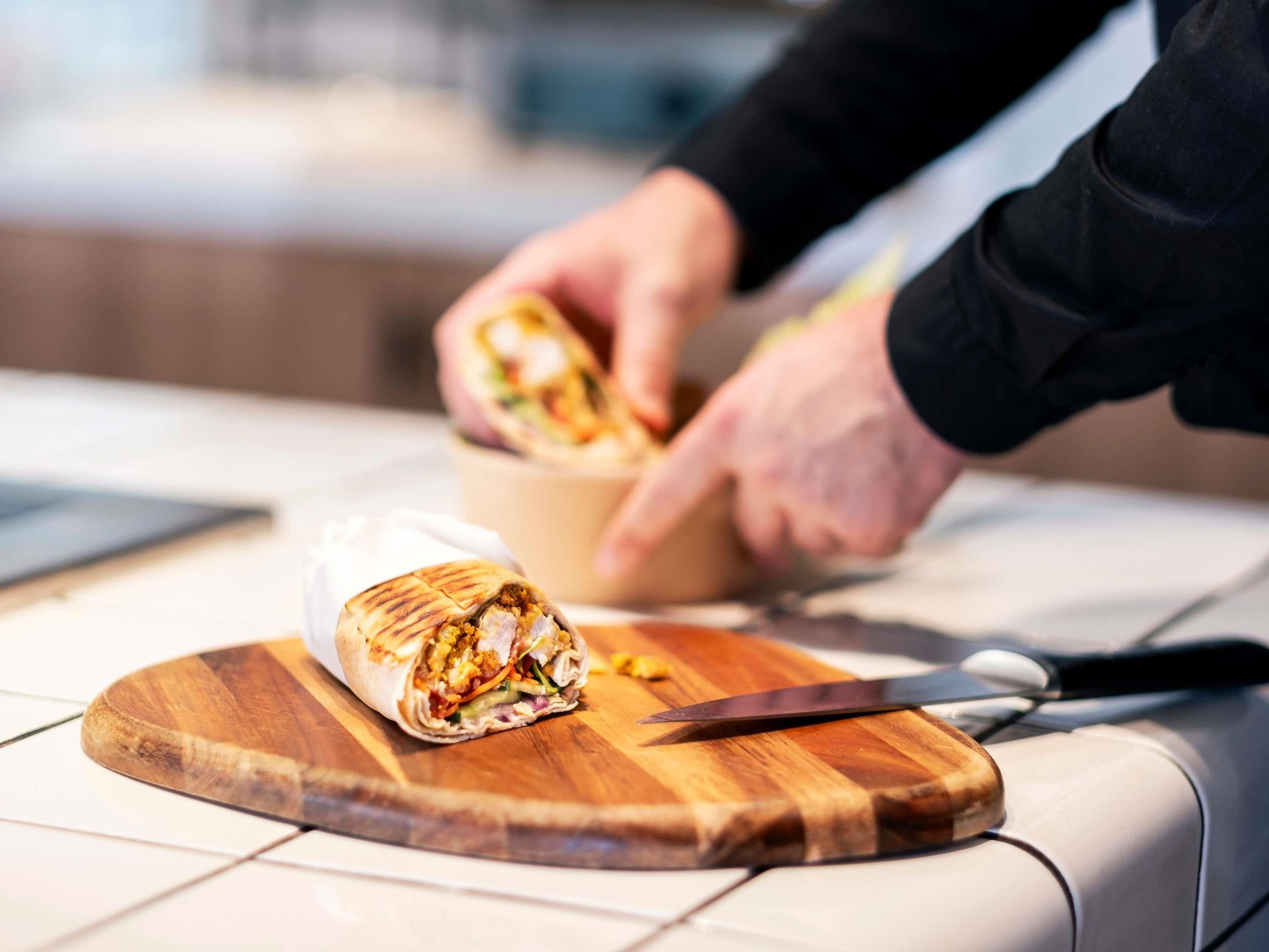 Alguém preparando um wrap em uma tábua de madeira.