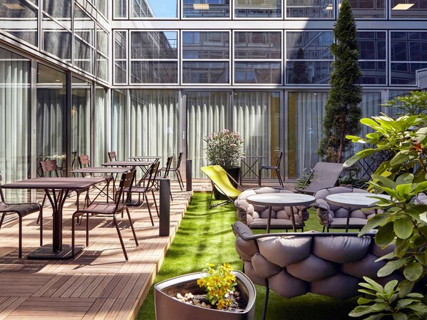 Relax in the hotel's outdoor patio area, featuring a dining table, lounge seating, and a small garden.