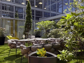 A modern outdoor seating area with a stone wall, green lawn, and potted plants. - Mercure Paris La Défense Grande Arche (Nanterre)