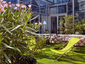 A modern outdoor seating area with a glass building in the background. - Mercure Paris La Défense Grande Arche (Nanterre)