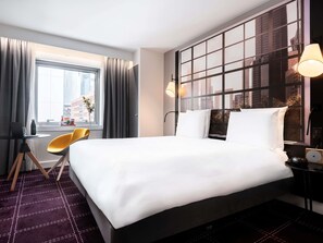 A hotel room with a large bed, a desk with a chair, a window with curtains, and a city view. - Mercure Paris La Défense Grande Arche (Nanterre)