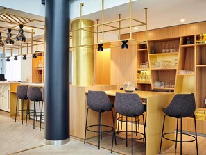 A modern bar area with a central column, bar stools, and shelves with glasses and bottles. - Mercure Paris La Défense Grande Arche (Nanterre)