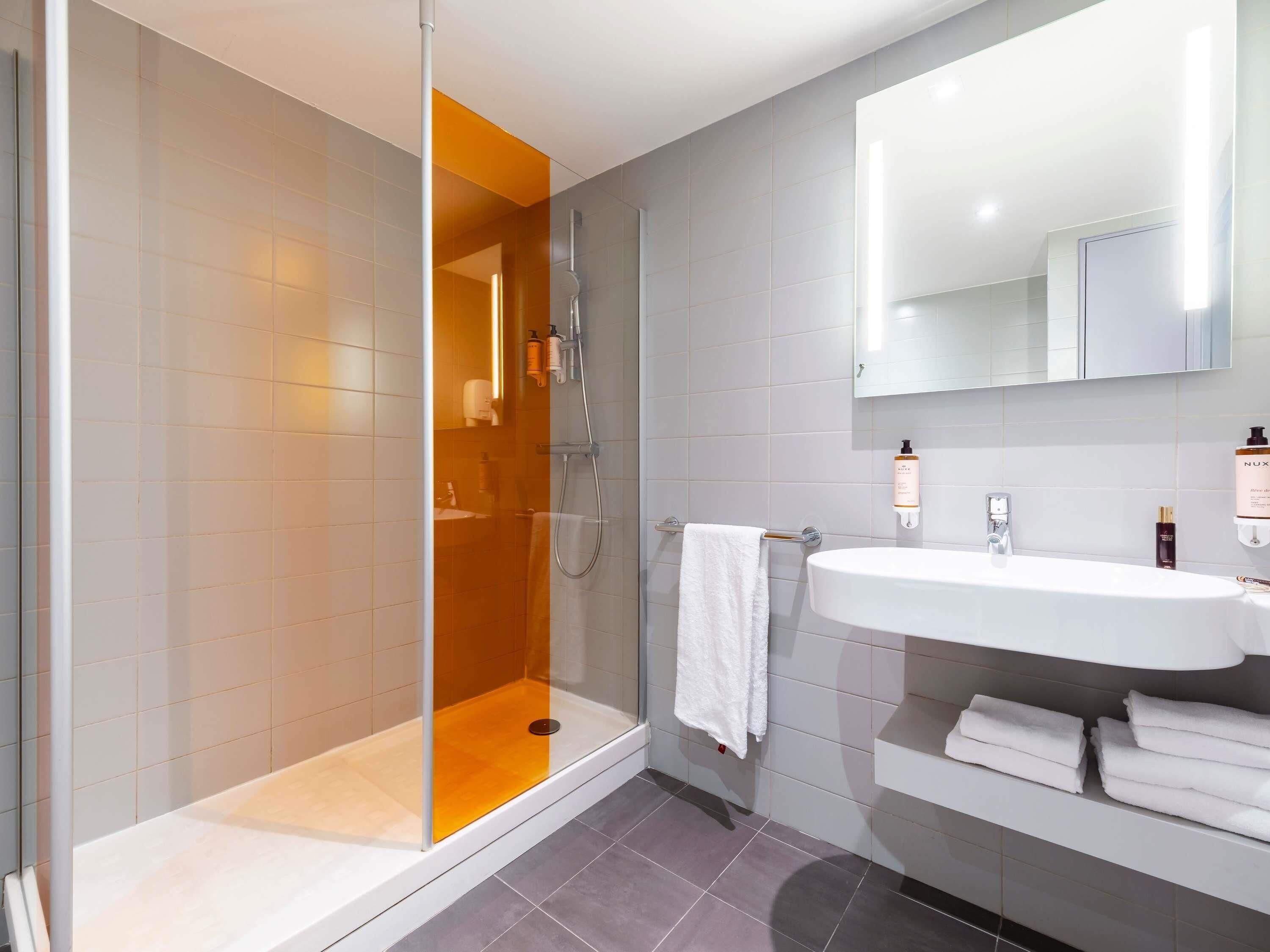 A modern bathroom with a glass-enclosed shower, a white sink, and a mirror above it.